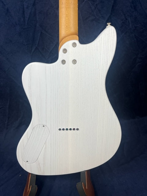 White electric guitar back with visible wood grain, bolt-on neck, three neck screws, string ferrules, and an oval electronics cover on the lower left.