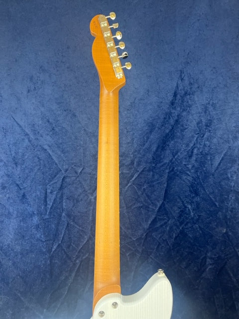 Electric guitar photographed from the back, showing a maple neck, six tuning pegs, and part of the white body against a textured blue background.