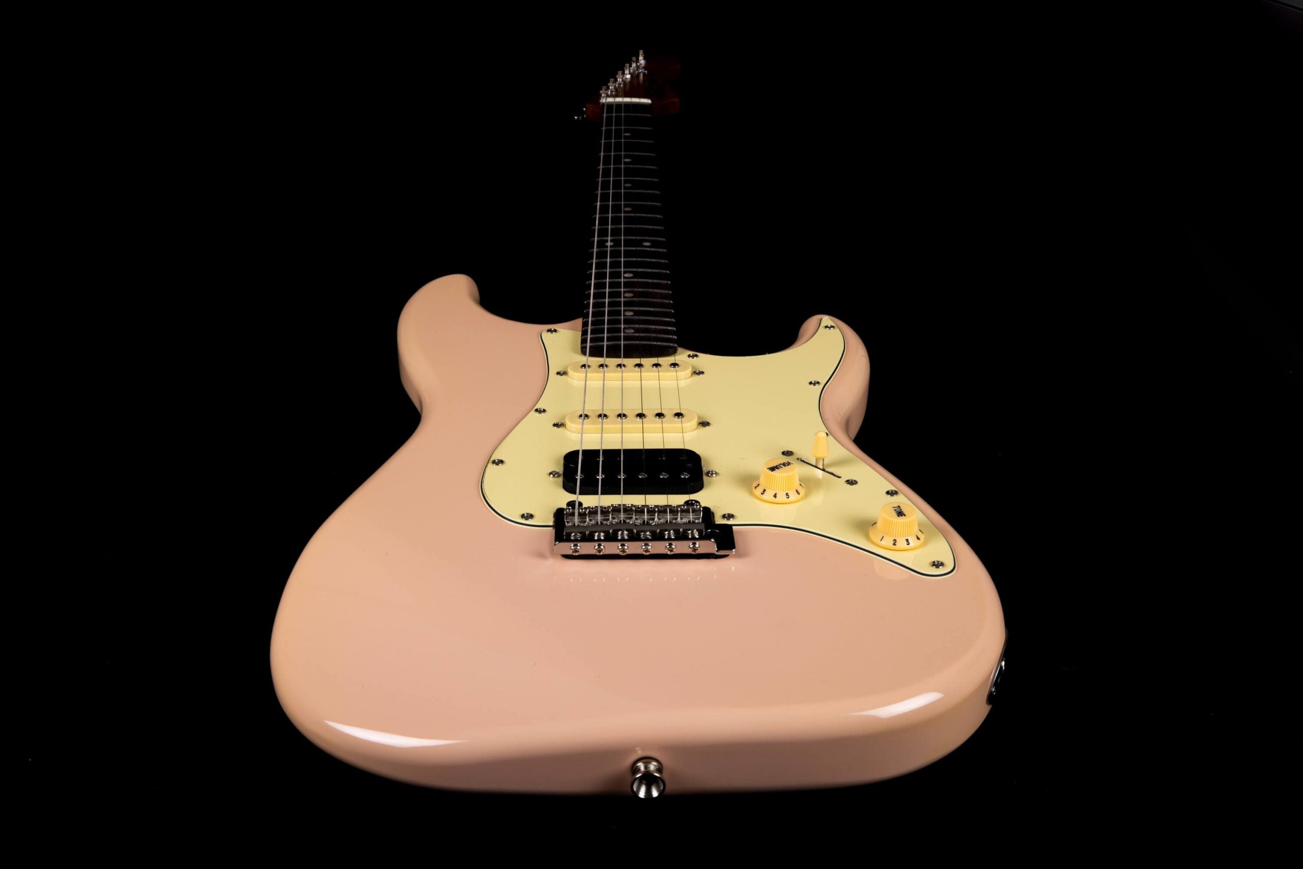 Glossy light pink electric guitar with a cream pickguard, three pickups, chrome bridge, and yellow control knobs, viewed from the body end.