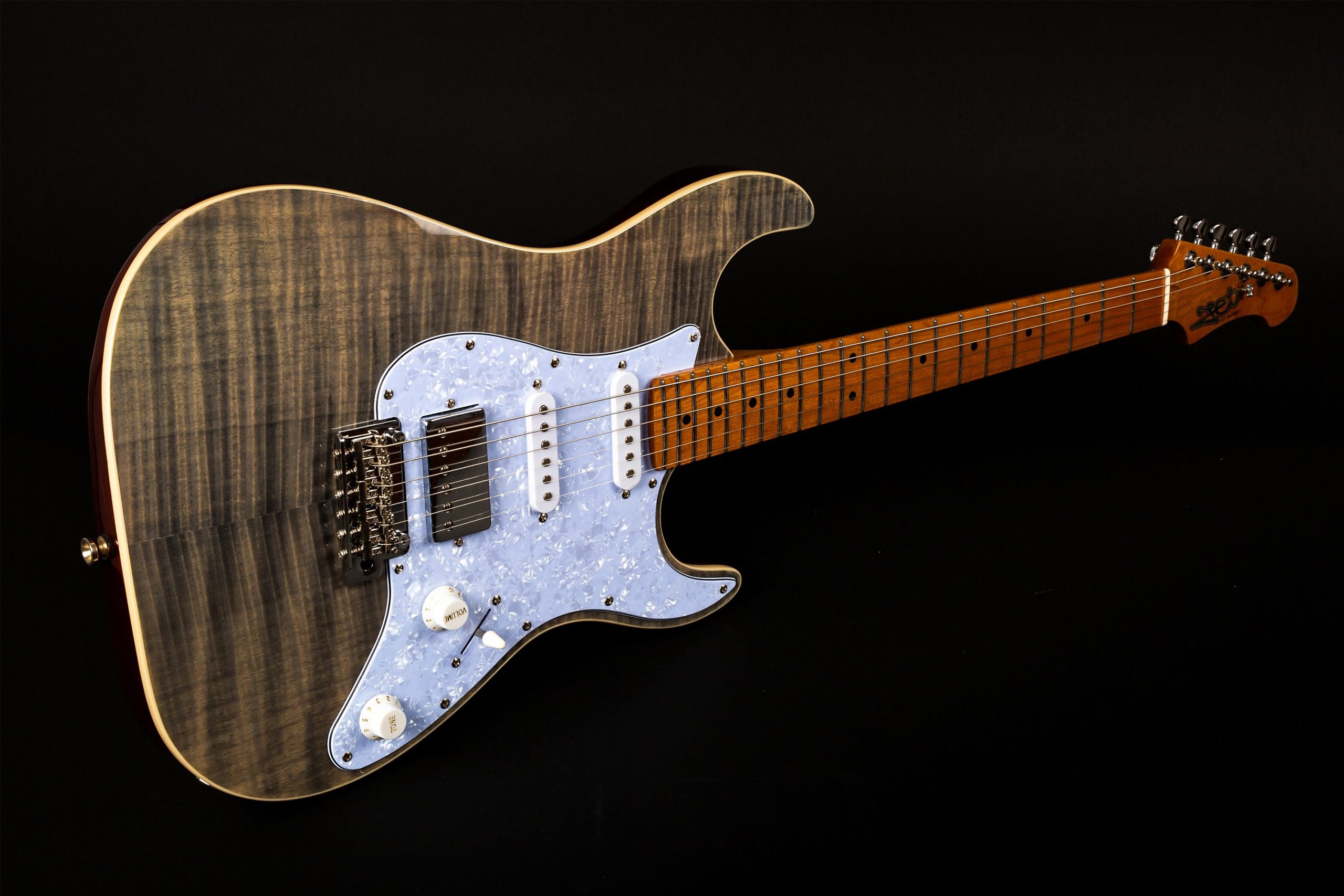 Electric guitar with a grey flamed wood finish, pearl-white pickguard, three pickups, two white knobs, and a dark maple fretboard with dot inlays.