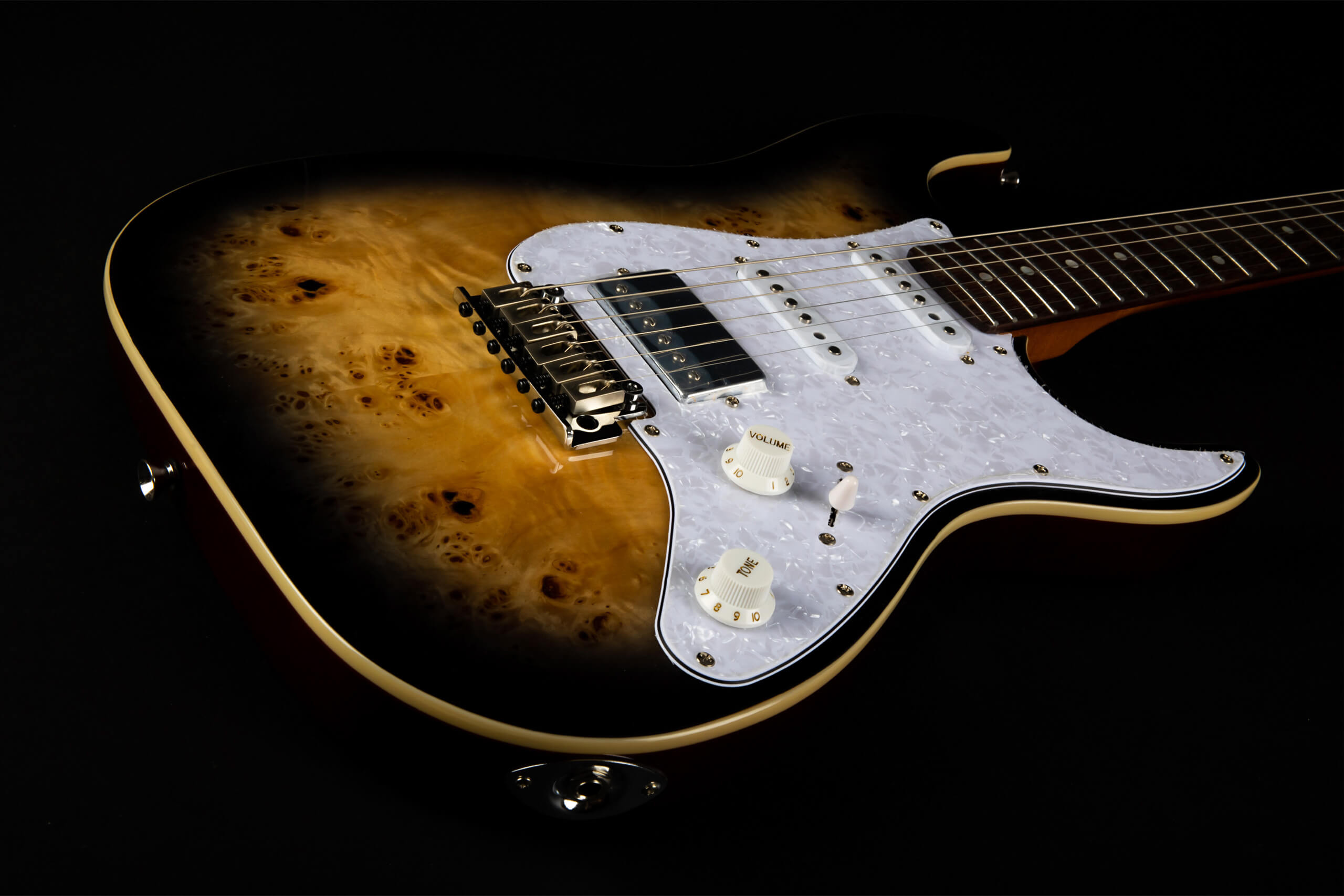 Electric guitar with a glossy, natural wood burl top, black burst edges, white pearloid pickguard, chrome bridge, and two white control knobs.