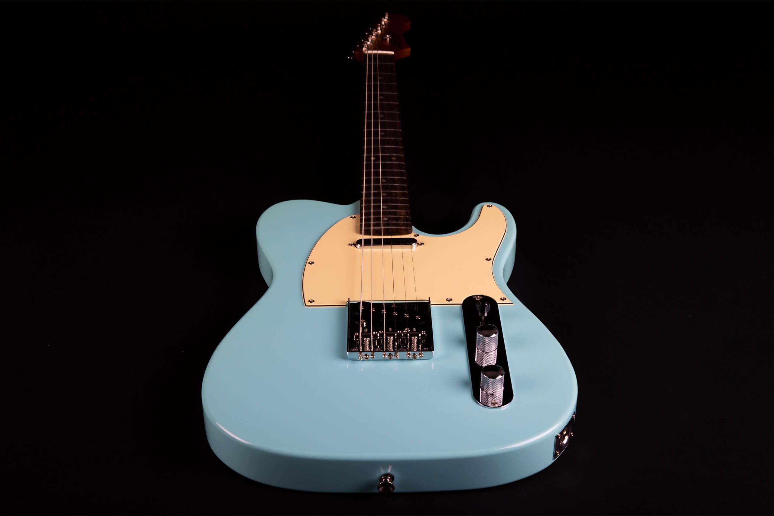 Light blue electric guitar with a cream pickguard, chrome bridge, and two chrome control knobs, viewed from the body end against a black background.