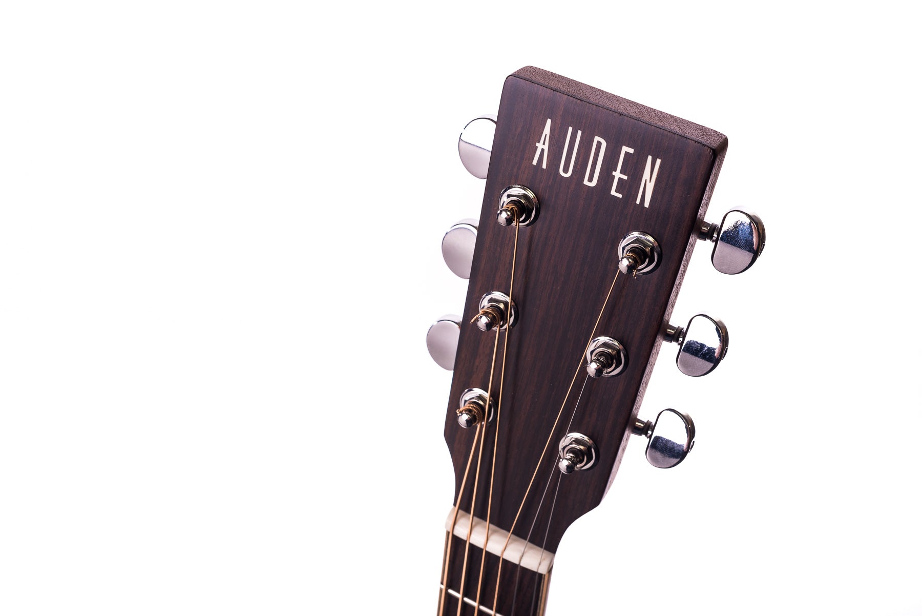 Close-up of an acoustic guitar headstock with six tuning pegs and the brand name "Auden" in white letters on dark wood.