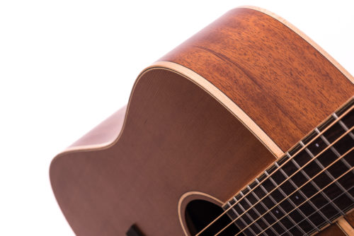 A close-up of an acoustic guitar’s body and fretboard, showing smooth brown wood with light trim along the edge.