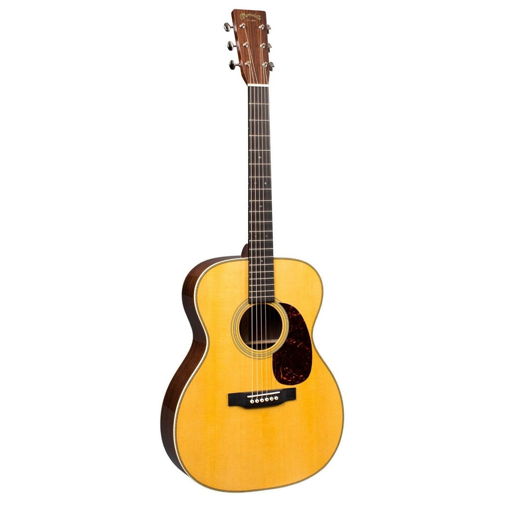 Acoustic guitar with a natural wood finish, dark fingerboard, round body, six strings, and a dark brown pickguard beside the sound hole.
