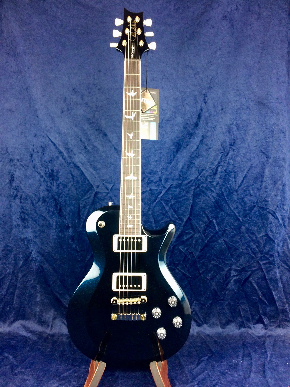 Glossy black electric guitar with two humbucker pickups, four control knobs, and bird inlays on the fretboard, set against a blue background.