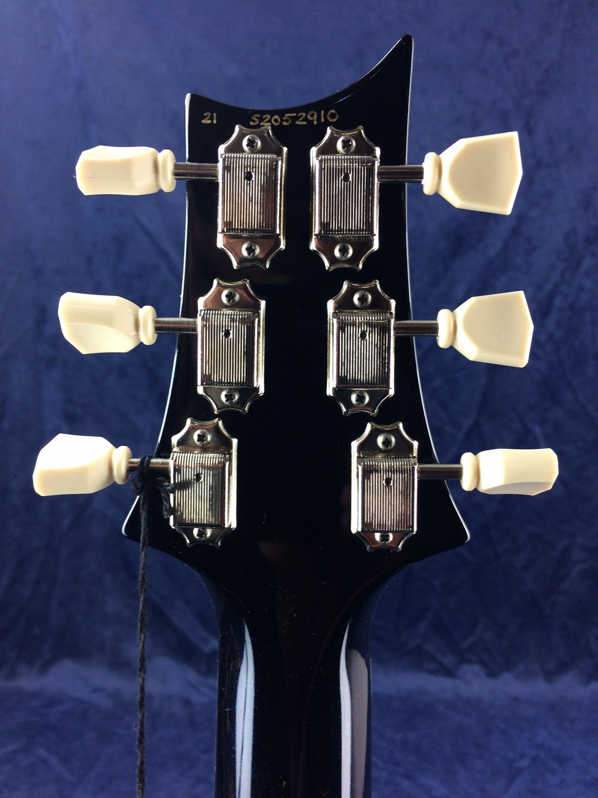 Six vintage-style tuning pegs with white knobs on a black electric guitar headstock, serial number 52052910 engraved above the tuners.