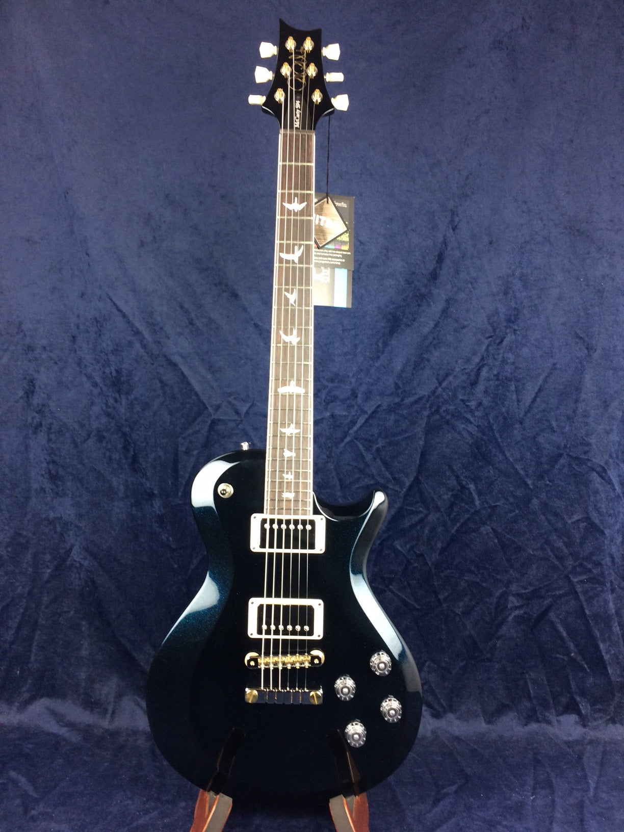 Glossy dark blue electric guitar with two humbucker pickups, four control knobs, bird inlays on the fretboard, and white tuning pegs.