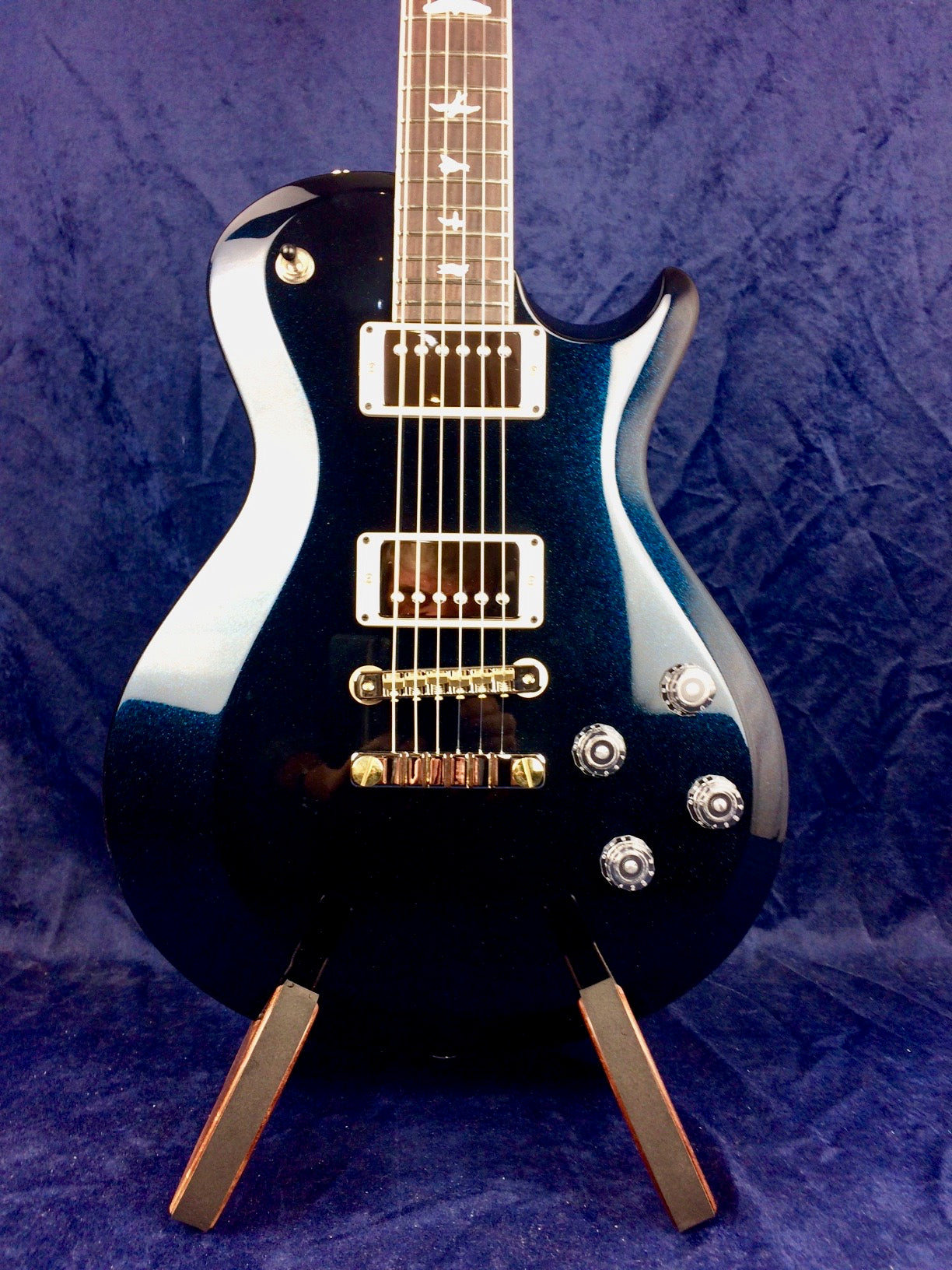 Glossy dark blue electric guitar with chrome hardware, two humbucker pickups, four control knobs, and bird inlays on the fretboard.