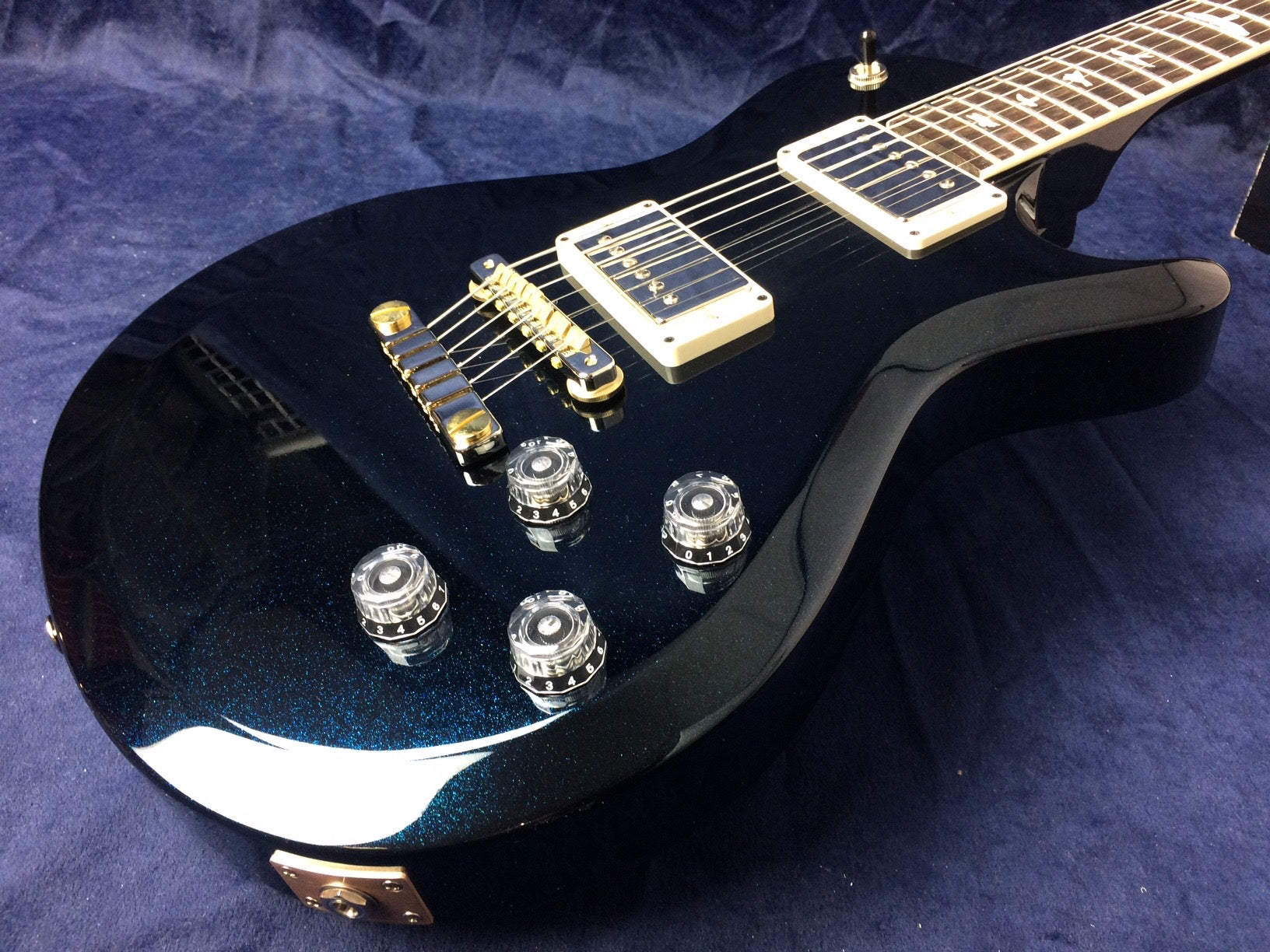 Glossy dark blue electric guitar with four clear control knobs, gold bridge, two humbucker pickups, and a rosewood fretboard.