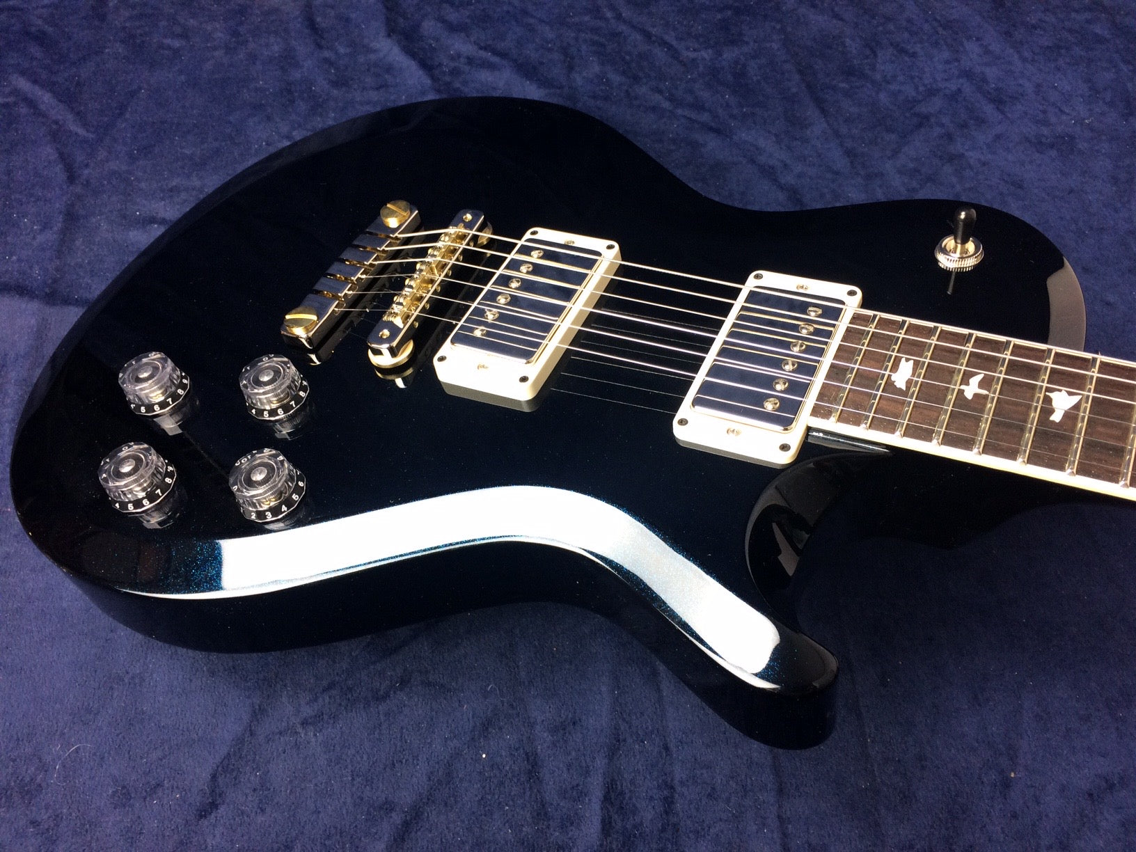 Glossy black electric guitar with four black control knobs, gold bridge, two humbucker pickups, and bird inlays on the fretboard.