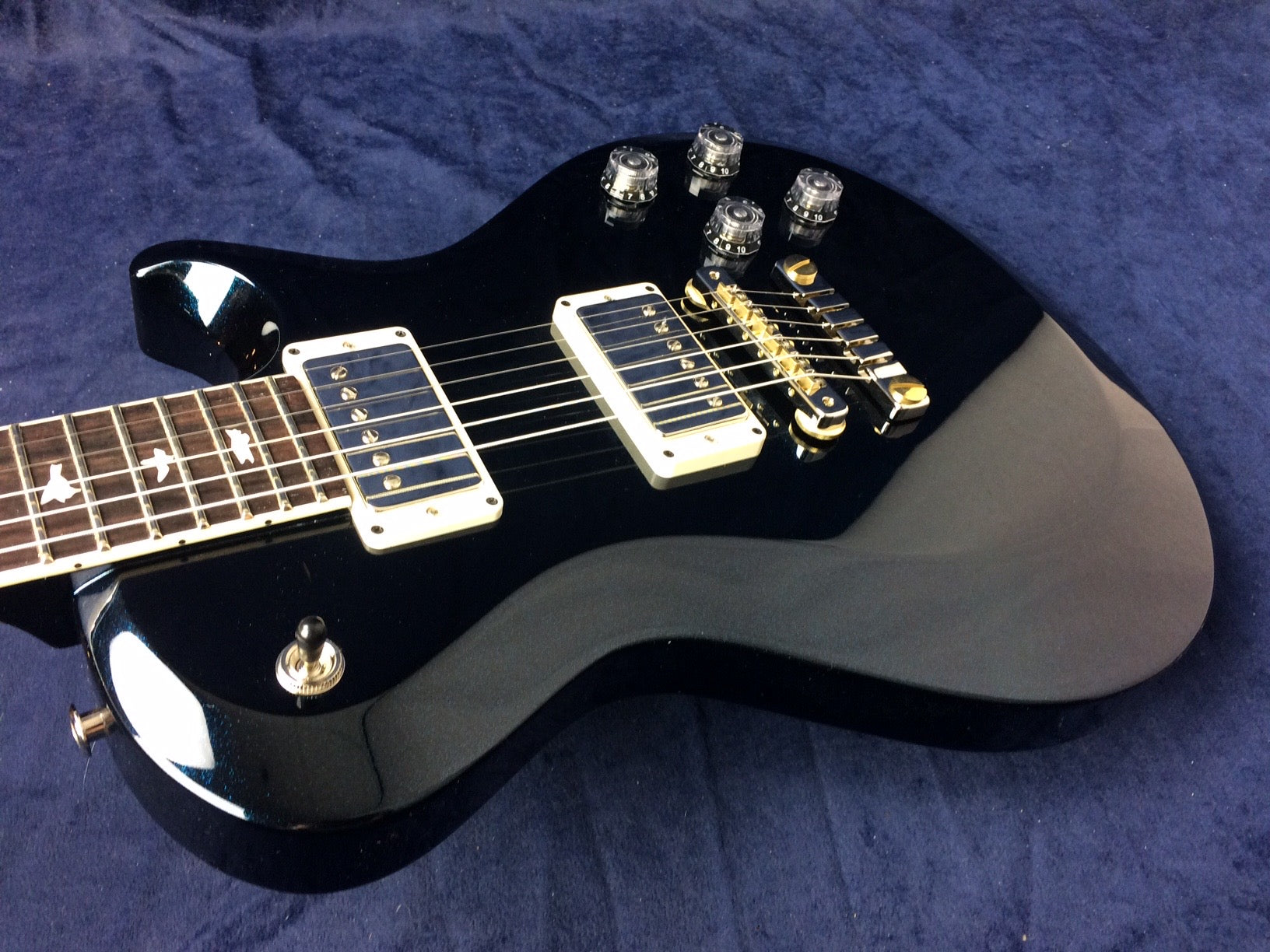 Glossy black electric guitar with two chrome humbucker pickups, four clear control knobs, gold bridge, and bird inlays on the fretboard.