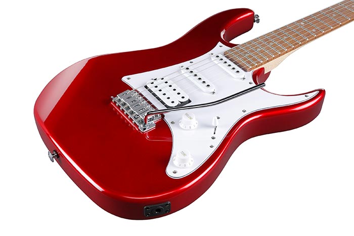 Red electric guitar with a white pickguard, three pickups, two control knobs, and a whammy bar. The fretboard is a light wood color.