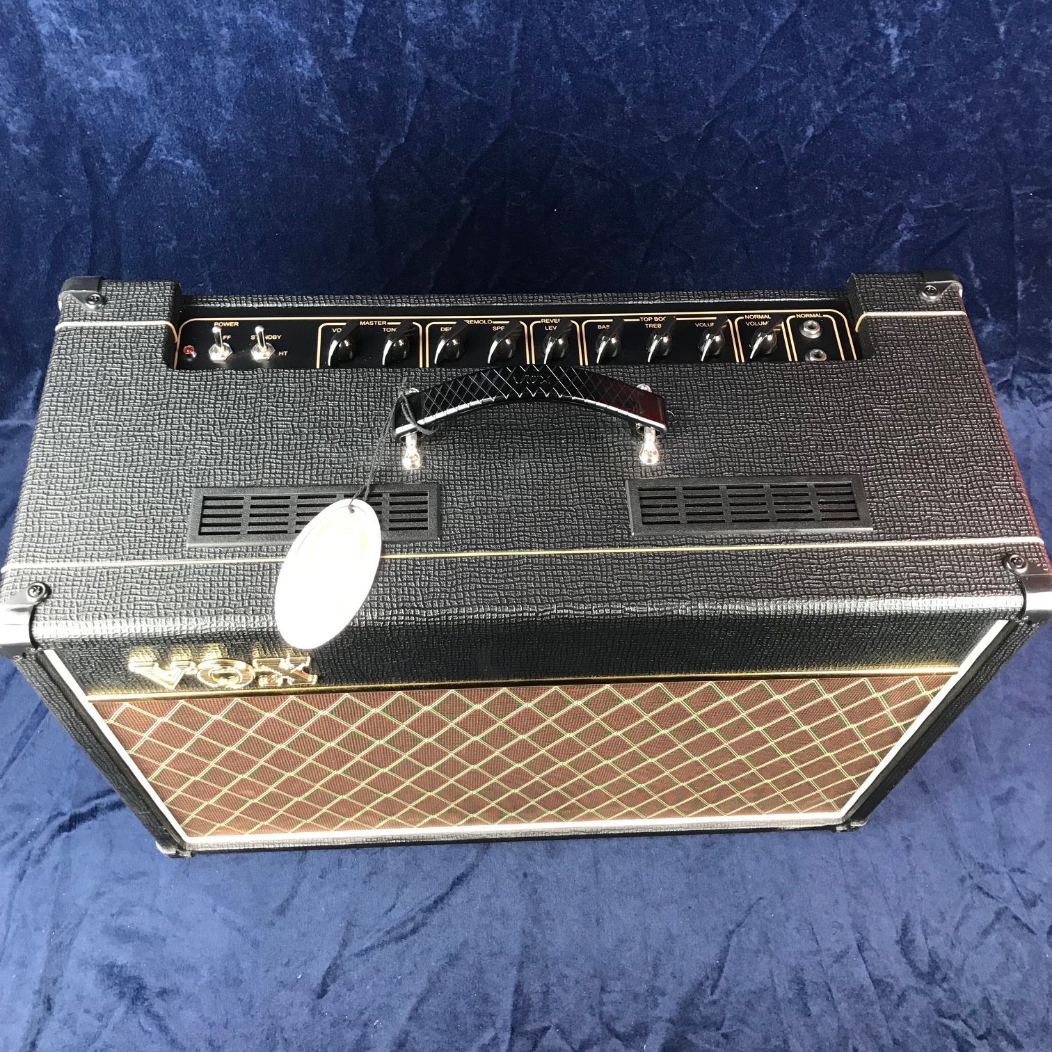 Amplificateur Vox noir avec grille avant brun à motif losange doré, poignée sur le dessus, plusieurs boutons de réglage en façade supérieure.
