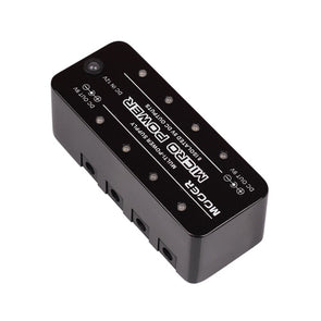 Black effects pedal power supply unit with multiple DC output ports along one side and labeled indicators on the top panel.