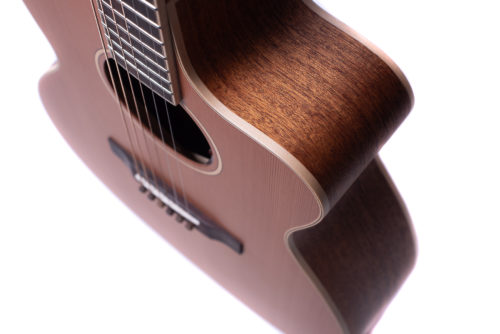 Curved wooden body of an acoustic guitar with six strings, visible soundhole, and bridge, photographed from an angled top side view.