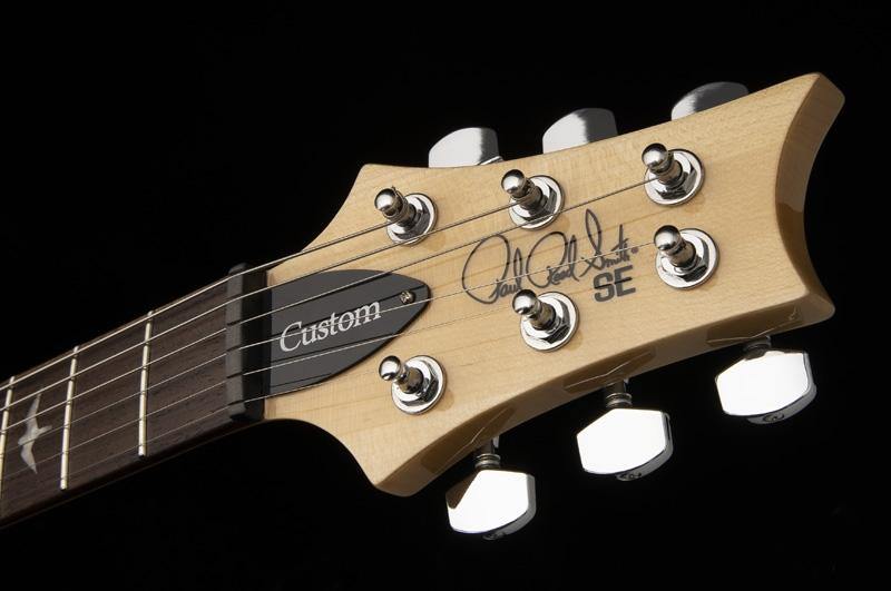 Light wood electric guitar headstock with six chrome tuning pegs, "Custom" label, and signature with "SE" printed near the top.