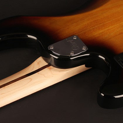 Close-up of a bass guitar neck joint, showing a light wood neck attached to a glossy sunburst body with a metal plate and screws.